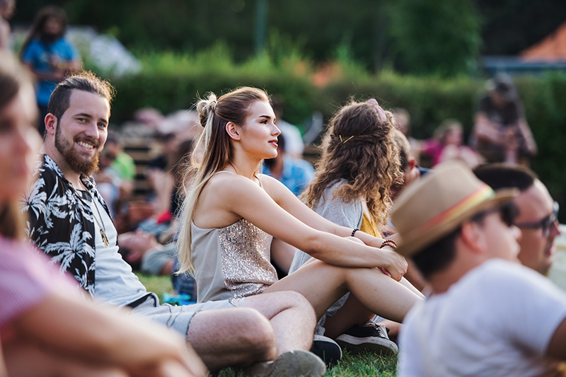 Group of young friends sitting on ground at summer festival.